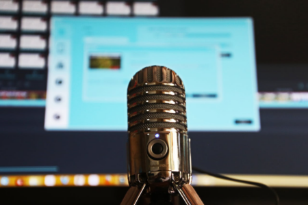 Image: a powered-on USB microphone sits in front of a computer monitor