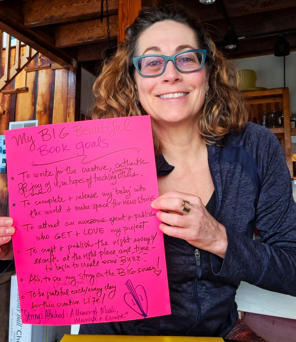 Anne Marina Pellicciotto holding a neon pink piece of paper on which is a written a list of goals and titled "My Big Beautiful Book Goals."