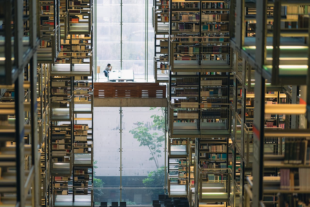 Image: at a library in Ciudad de México, the floor is so highly polished that the book stacks and windows are reflected, creating a somewhat surreal and confusing scene. A single visitor is seated at a table in the center.