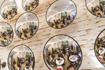 Image: from a seat at a cafe, a photographer shoots a photo of the numerous circular mirrors on the wall that reflect both herself and several dozen other patrons.