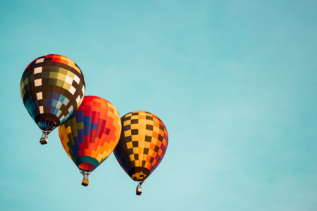 Image: Three hot-air balloons fly in a tight cluster against a blue sky.