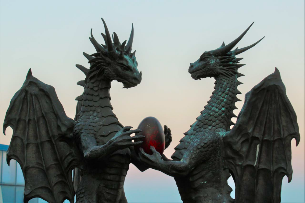 Image: a statue in Busan, South Korea of two standing dragons; one holds forth a red egg to the other.