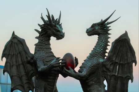 Image: a statue in Busan, South Korea of two standing dragons; one holds forth a red egg to the other.