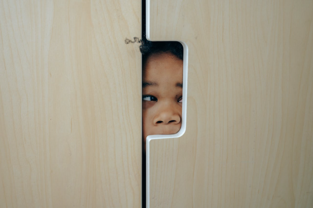Image: a child peeks out through the contour-cut handle in a set of doors.