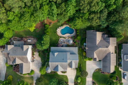 Image: aerial view of several suburban houses on a leafy street, only one of which has a swimming pool in the back yard.