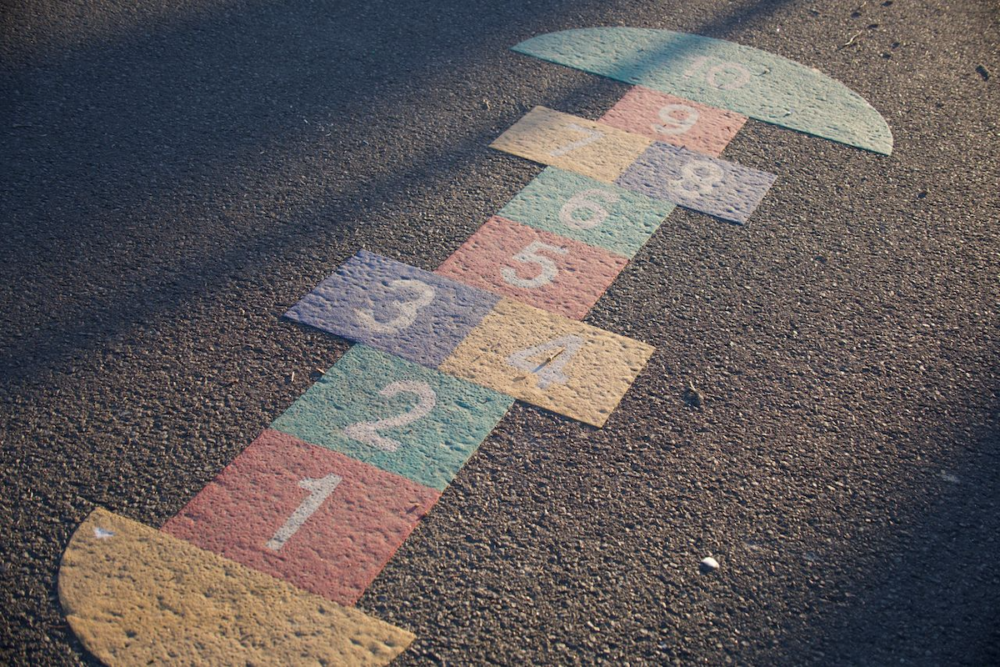 Image: a colorful hopscotch pattern painted on the concrete of a playground