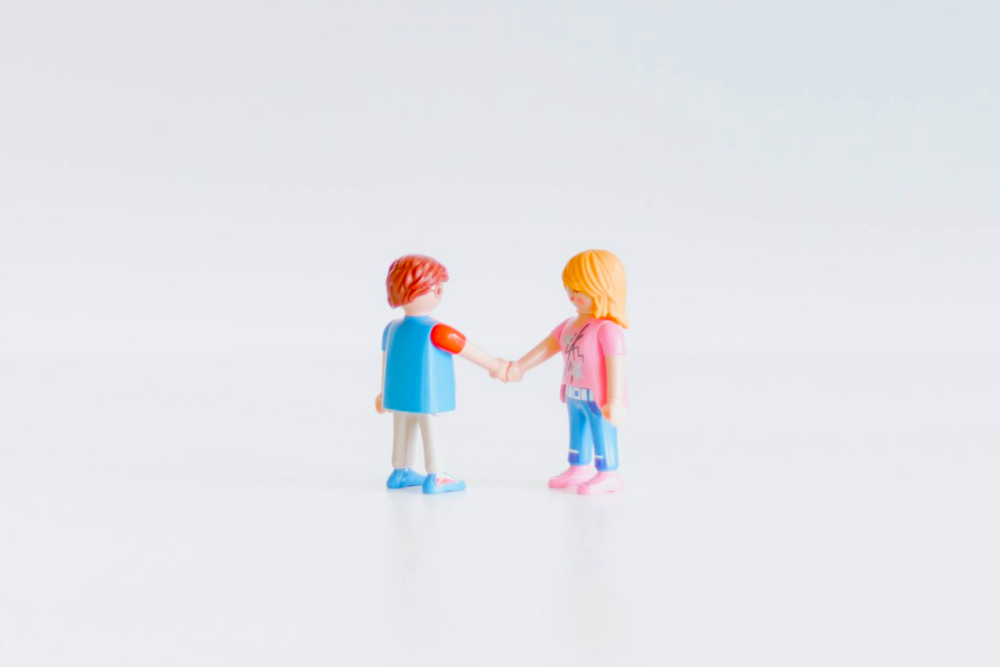 Image: two miniature toy figures appear to be shaking hands as if forging an agreement.