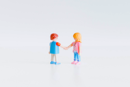 Image: two miniature toy figures appear to be shaking hands as if forging an agreement.